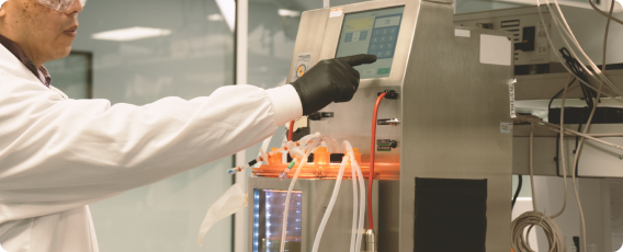 A man wearing a white coat and black gloves works with a piece of laboratory equipment.